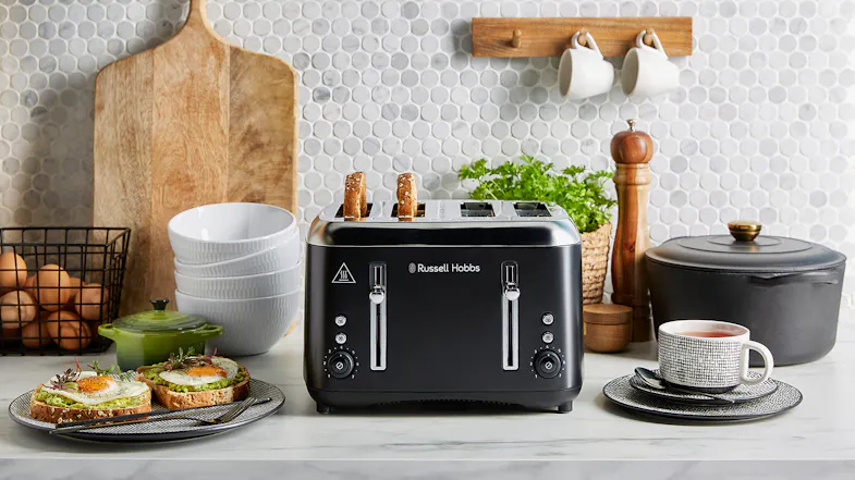 A black Russell Hobbs four‑slot toaster on a kitchen counter with toast popping up, surrounded by dishes and food A black Russell Hobbs four‑slot toaster on a kitchen counter with toast popping up, surrounded by dishes and food