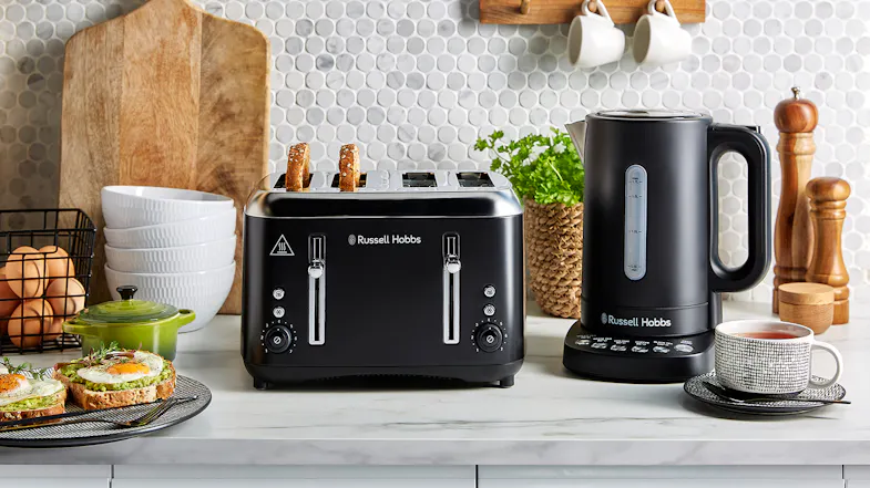 A black four‑slot toaster and matching electric kettle on a kitchen counter with breakfast items A black four‑slot toaster and matching electric kettle on a kitchen counter with breakfast items