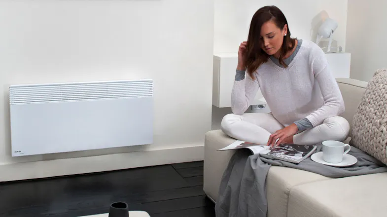 A person reading on a sofa next to a wall-mounted panel heater A person reading on a sofa next to a wall-mounted panel heater