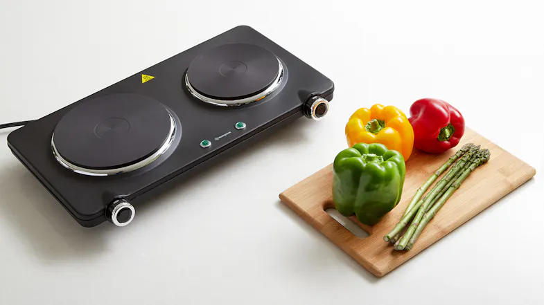 Dual hot plate next to a wooden cutting board with peppers and asparagus Dual hot plate next to a wooden cutting board with peppers and asparagus