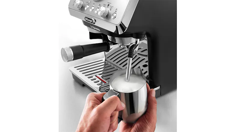 A Hand frothing milk with an espresso machine’s steam wand over a metal pitcher A Hand frothing milk with an espresso machine’s steam wand over a metal pitcher