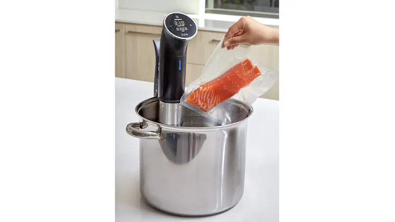 A hand lowering a vacuum-sealed salmon fillet into a water bath heated by the Westinghouse Sous Vide A hand lowering a vacuum-sealed salmon fillet into a water bath heated by the Westinghouse Sous Vide