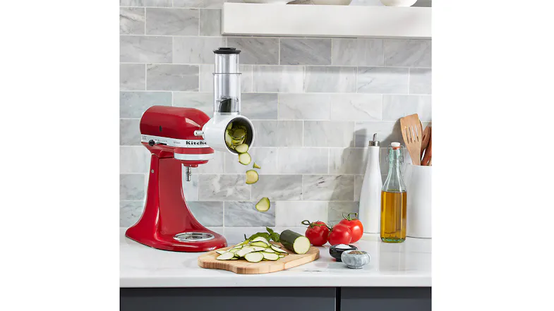 Red stand mixer with slicer attachment on a kitchen counter slicing zucchini onto a wood board Red stand mixer with slicer attachment on a kitchen counter slicing zucchini onto a wood board