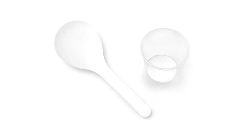 A white plastic spoon is placed next to a small, clear plastic cup A white plastic spoon is placed next to a small, clear plastic cup