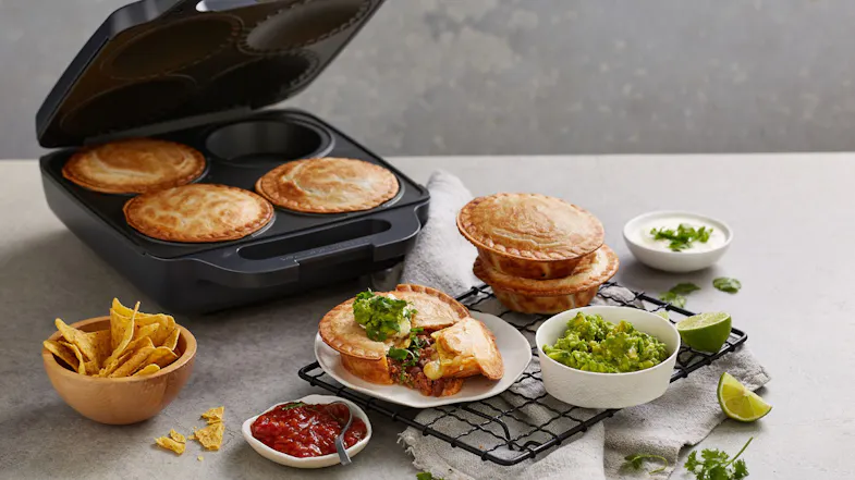 Sunbeam Pie Magic 4 pie maker on a counter with cooked pies, served plates, salsa, chips, and guacamole arranged for a meal Sunbeam Pie Magic 4 pie maker on a counter with cooked pies, served plates, salsa, chips, and guacamole arranged for a meal