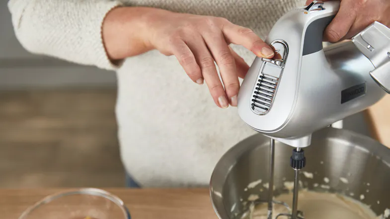 Person pressing the release button on the Kenwood Chefette handheld mixer while mixing batter in the bowl Person pressing the release button on the Kenwood Chefette handheld mixer while mixing batter in the bowl