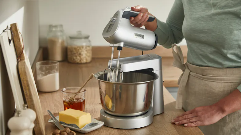 Person using the handheld mixer while it is attached to the stand, mixing ingredients in the bowl Person using the handheld mixer while it is attached to the stand, mixing ingredients in the bowl