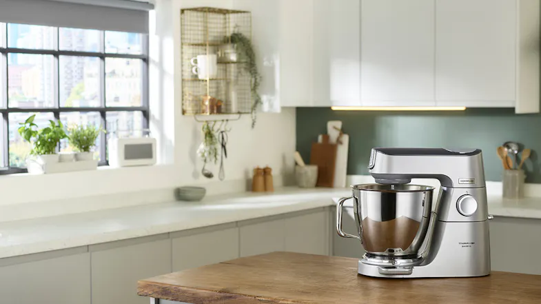 Kenwood Titanium Chef Baker XL stand mixer in silver positioned on a wooden countertop in a bright kitchen Kenwood Titanium Chef Baker XL stand mixer in silver positioned on a wooden countertop in a bright kitchen