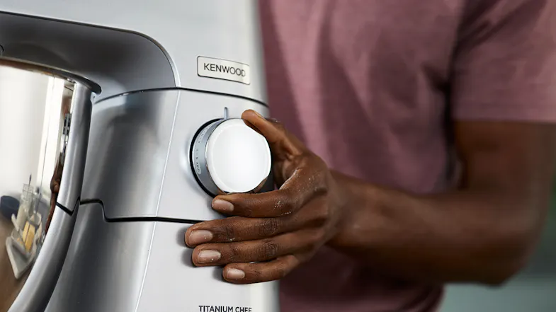 Close‑up of a hand adjusting the speed control dial on the silver Kenwood Titanium Chef Baker XL stand mixer Close‑up of a hand adjusting the speed control dial on the silver Kenwood Titanium Chef Baker XL stand mixer