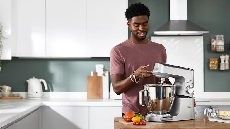 Person lifting the head of the silver Titanium Chef Baker XL stand mixer while preparing ingredients on a kitchen counter Person lifting the head of the silver Titanium Chef Baker XL stand mixer while preparing ingredients on a kitchen counter