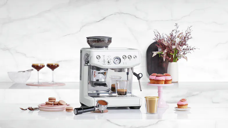 A white espresso machine and desserts on a marble counter, with cups, a portafilter, and decorative elements A white espresso machine and desserts on a marble counter, with cups, a portafilter, and decorative elements