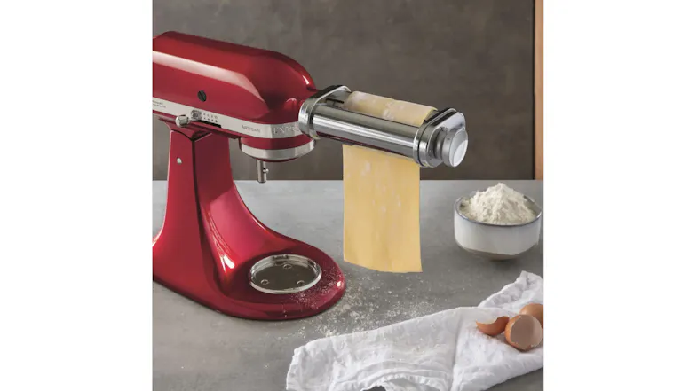 KitchenAid mixer with pasta roller in a kitchen setting next to flour and eggshells on a countertop KitchenAid mixer with pasta roller in a kitchen setting next to flour and eggshells on a countertop