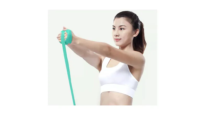 Person performing an upper-body exercise using a green resistance band while wearing a white sports top Person performing an upper-body exercise using a green resistance band while wearing a white sports top