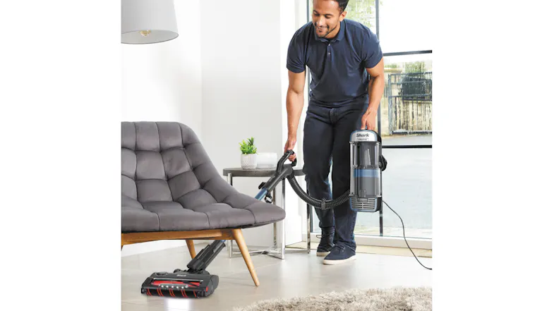 Person cleaning tight spaces under a chair using a lift‑away vacuum with a hose attachment Person cleaning tight spaces under a chair using a lift‑away vacuum with a hose attachment