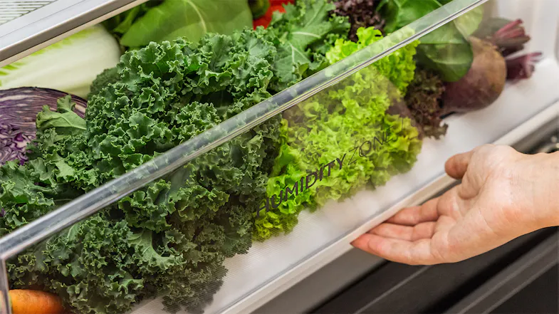 A hand opening the Haier Humidity Zone bin to access fresh vegetables A hand opening the Haier Humidity Zone bin to access fresh vegetables