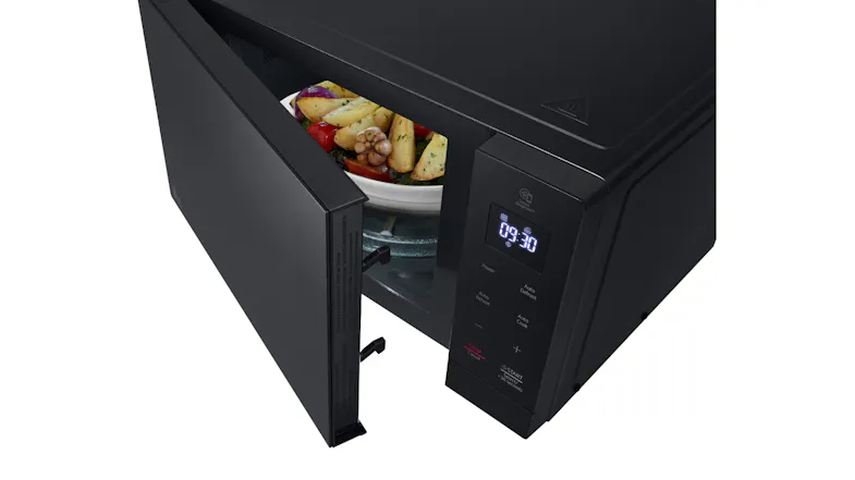 Top‑view of a black microwave with an open door and a bowl of mixed vegetables inside Top‑view of a black microwave with an open door and a bowl of mixed vegetables inside