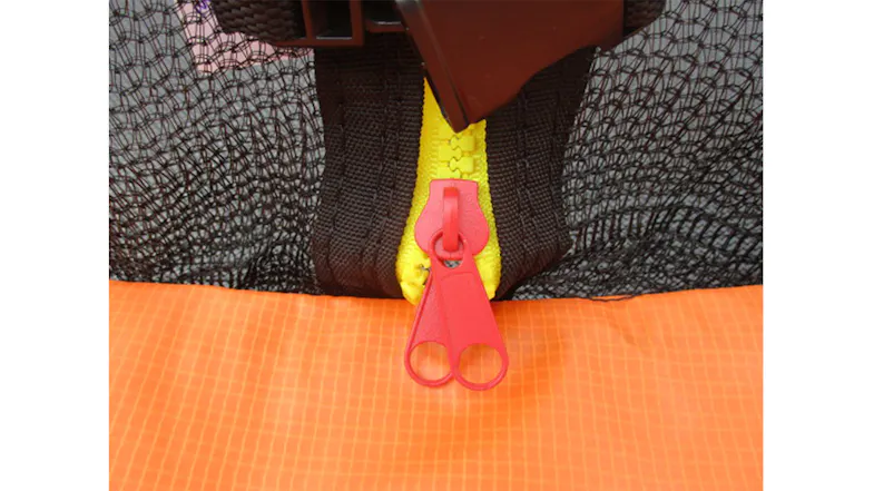 Close-up of a dual red zipper on a yellow track closing a trampoline safety net above an orange pad Close-up of a dual red zipper on a yellow track closing a trampoline safety net above an orange pad