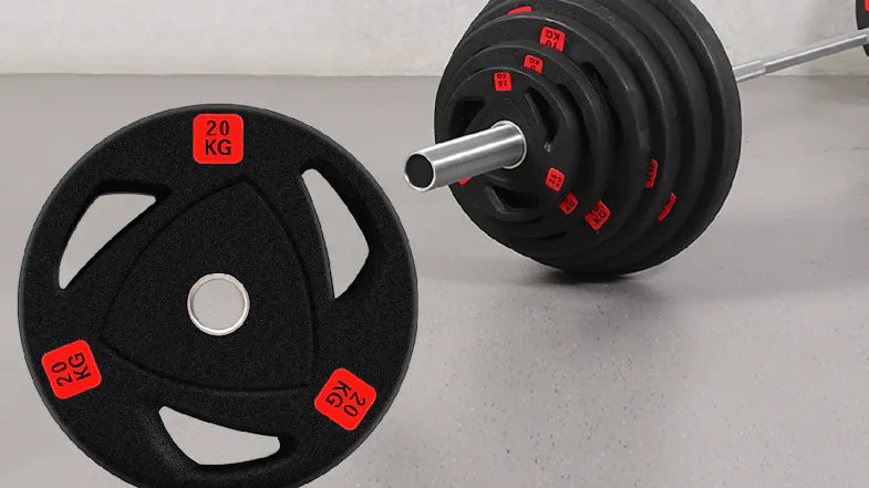 A black 20 kg PROTRAIN weight plate sits in the foreground next to a loaded barbell on a grey gym floor A black 20 kg PROTRAIN weight plate sits in the foreground next to a loaded barbell on a grey gym floor