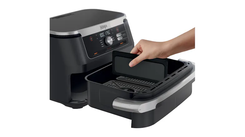 Hand placing a divider inside the open drawer of a Ninja air fryer with digital controls Hand placing a divider inside the open drawer of a Ninja air fryer with digital controls