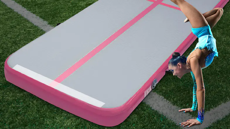 Athlete performing a handstand on a grey and pink inflatable air track mat on a grassy field Athlete performing a handstand on a grey and pink inflatable air track mat on a grassy field