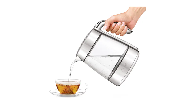 A hand tilting the Breville Smart Crystal Luxe glass kettle to pour hot water into a glass teacup on a saucer A hand tilting the Breville Smart Crystal Luxe glass kettle to pour hot water into a glass teacup on a saucer