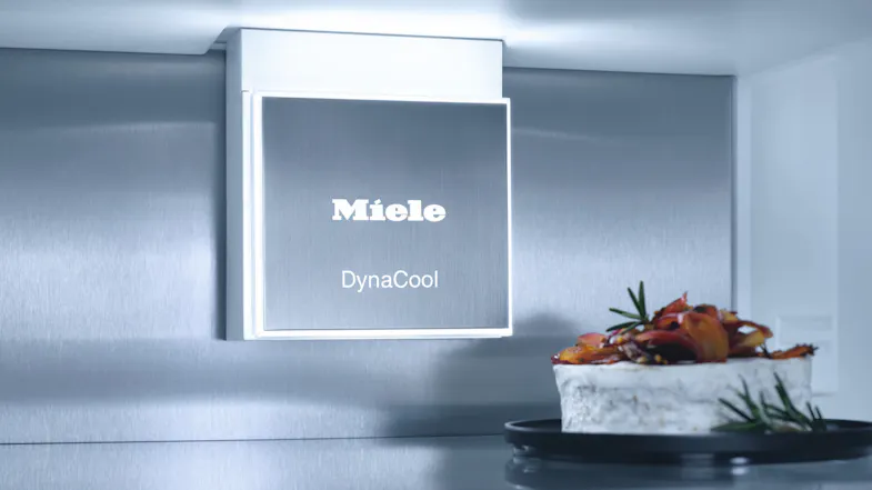Interior view of Miele fridge showing DynaCool system logo and a cake on a black plate Interior view of Miele fridge showing DynaCool system logo and a cake on a black plate