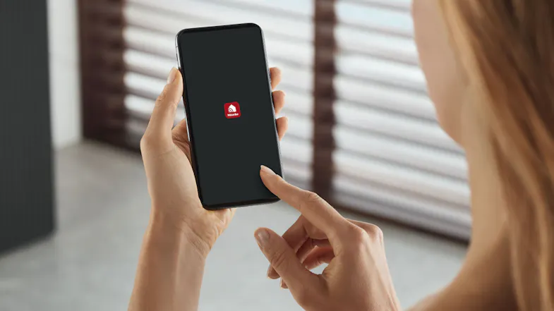 Person holding a smartphone with the Miele app icon displayed, indicating smart connectivity for fridge control Person holding a smartphone with the Miele app icon displayed, indicating smart connectivity for fridge control