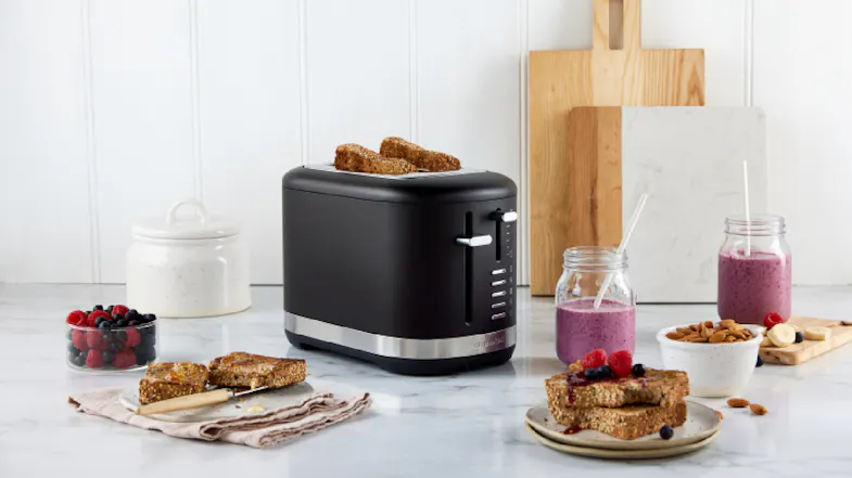 The toaster displayed on a marbled kitchen countertop along with some fruits, pastries, and honey The toaster displayed on a marbled kitchen countertop along with some fruits, pastries, and honey