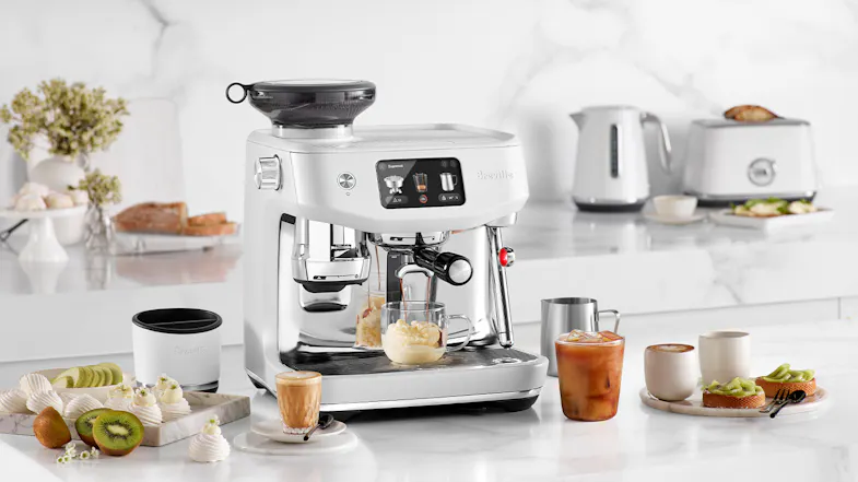 An espresso machine on a kitchen counter, surrounded by coffee drinks, pastries, and a fruit An espresso machine on a kitchen counter, surrounded by coffee drinks, pastries, and a fruit
