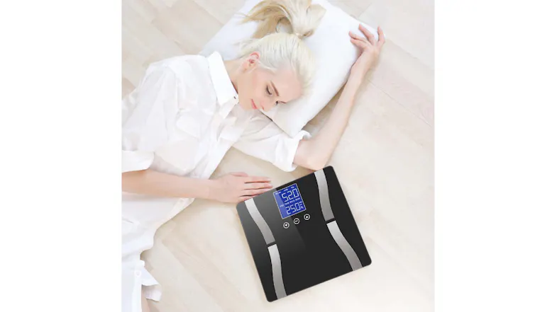 A person lying on the floor beside a digital weight scale displaying 52 kg and 25% body fat A person lying on the floor beside a digital weight scale displaying 52 kg and 25% body fat