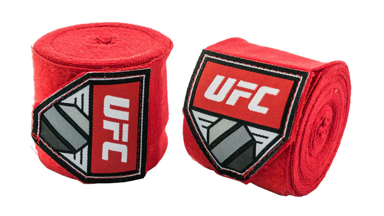 Two rolled red UFC hand wraps showing logo patches with white “UFC” text and a black-and-gray geometric pattern Two rolled red UFC hand wraps showing logo patches with white “UFC” text and a black-and-gray geometric pattern