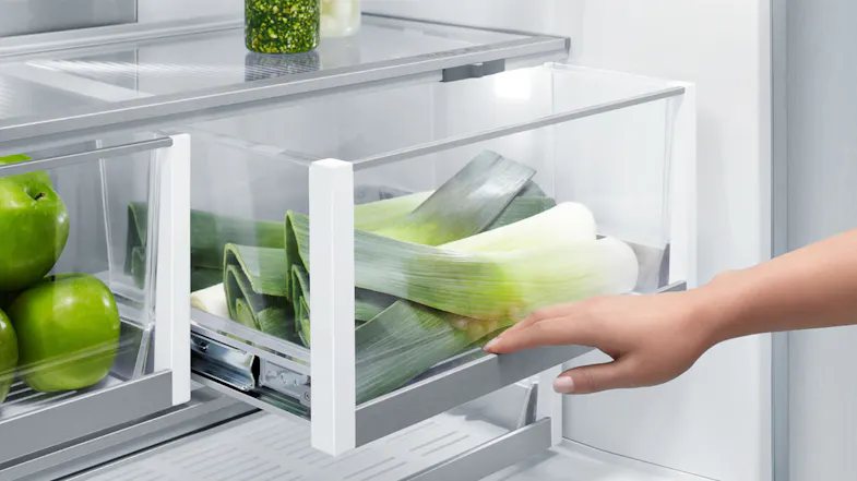 A hand pulling out a drawer to grab some vegetables A hand pulling out a drawer to grab some vegetables