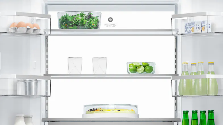 Interior view of a fridge showing shelves with eggs, butter, salad greens, limes, two glasses, a cake, and bottles Interior view of a fridge showing shelves with eggs, butter, salad greens, limes, two glasses, a cake, and bottles