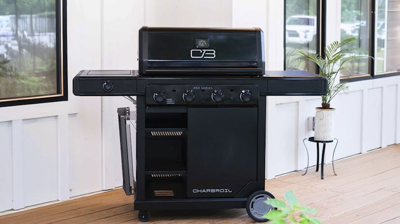 The BBQ is positioned on a wooden deck with the hood closed. The unit features four control knobs and storage The BBQ is positioned on a wooden deck with the hood closed. The unit features four control knobs and storage