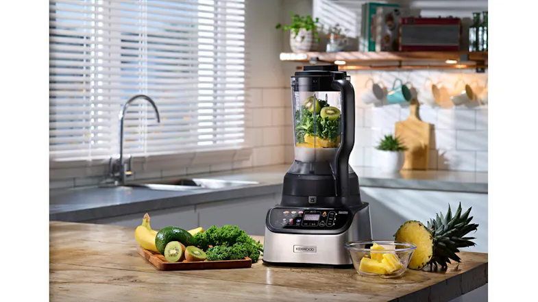 Food processor blending leafy greens, kiwi, and pineapple beside fresh produce on a wooden counter Food processor blending leafy greens, kiwi, and pineapple beside fresh produce on a wooden counter