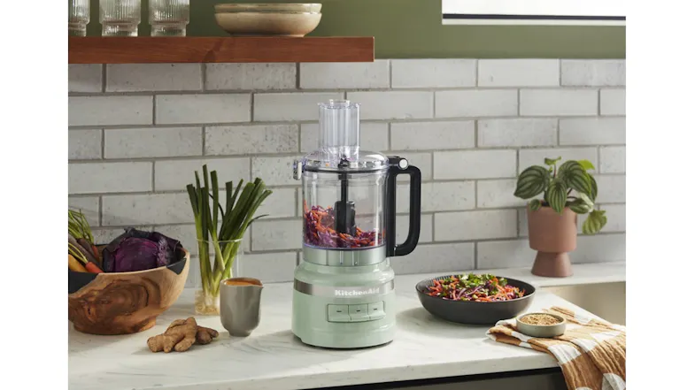 Light green KitchenAid food processor mixing vegetables in a modern kitchen setting Light green KitchenAid food processor mixing vegetables in a modern kitchen setting