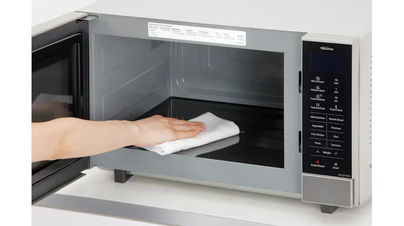 A person cleaning the microwave’s cooking chamber using a white cloth A person cleaning the microwave’s cooking chamber using a white cloth