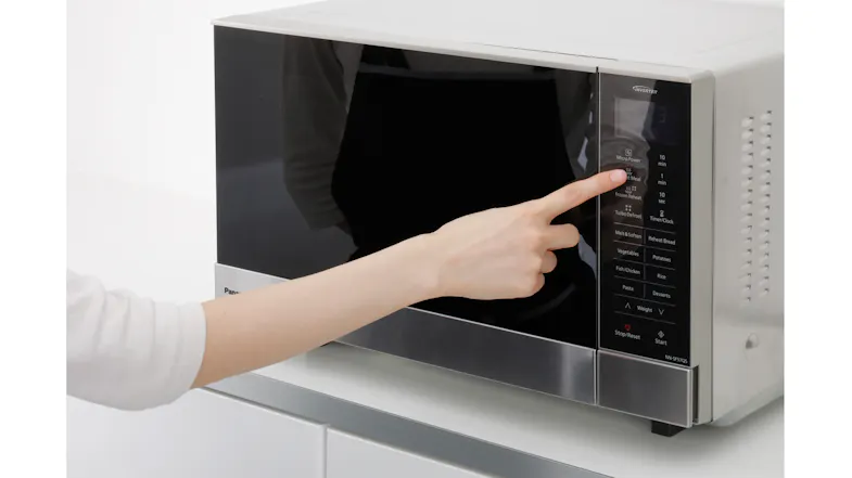 A hand pressing a button in a flatbed microwave oven A hand pressing a button in a flatbed microwave oven