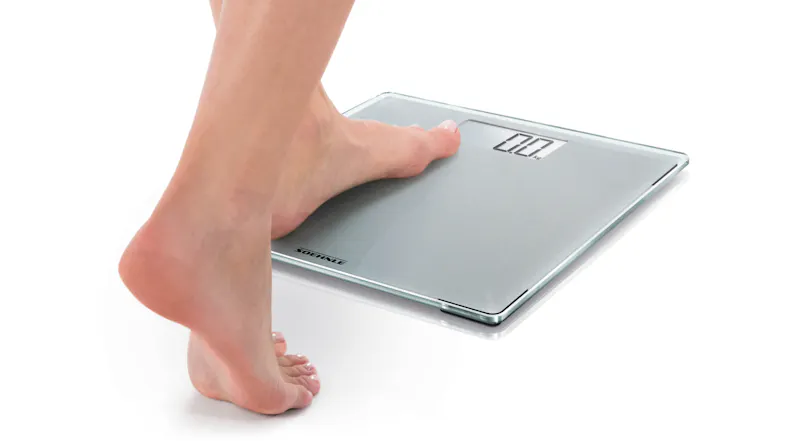 Foot stepping onto a digital bathroom scale with an LED display showing 0.0 kg Foot stepping onto a digital bathroom scale with an LED display showing 0.0 kg