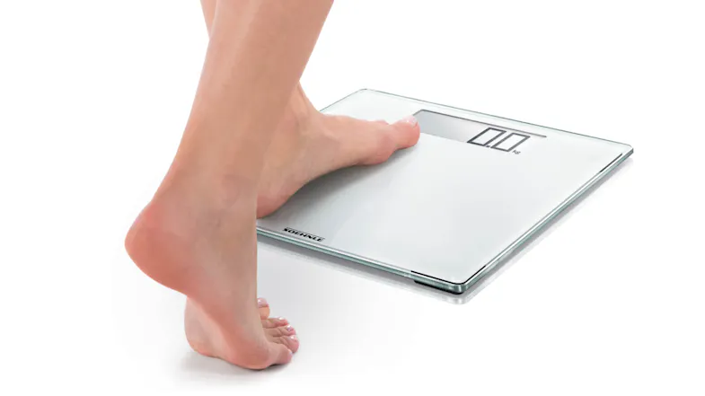 Foot stepping onto a digital bathroom scale with an LED display showing 0.0 kg Foot stepping onto a digital bathroom scale with an LED display showing 0.0 kg