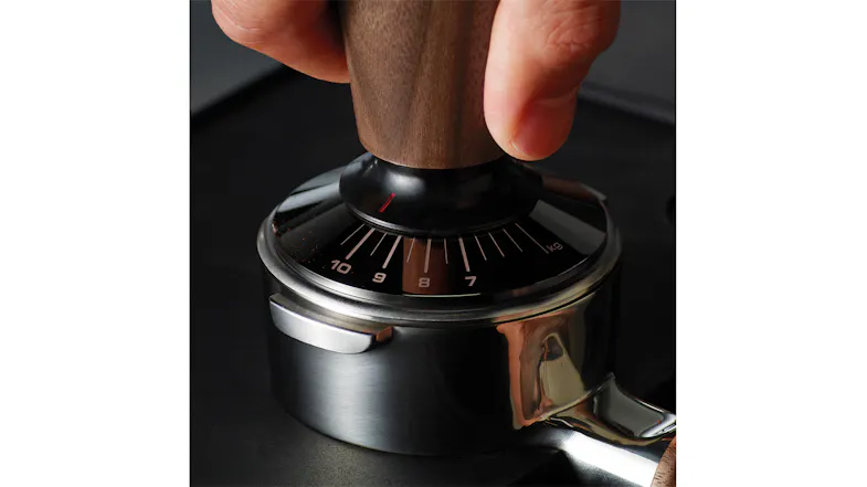 A close-up of a hand applying pressure with a tamper on ground coffee. A close-up of a hand applying pressure with a tamper on ground coffee.