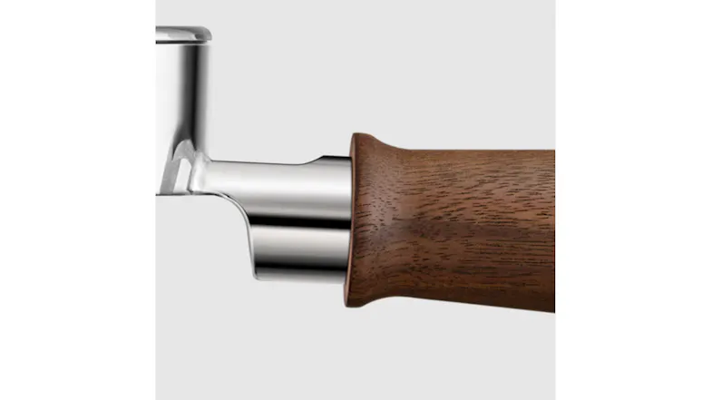 A close-up of the joint between the wooden handle and the metal head of the portafilter. A close-up of the joint between the wooden handle and the metal head of the portafilter.
