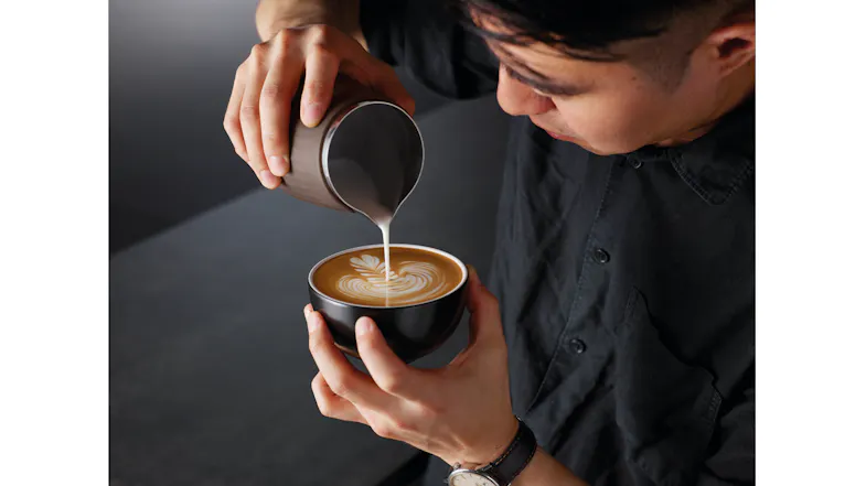 An overhead view of a person pouring milk from a jug into coffee to create latte art. An overhead view of a person pouring milk from a jug into coffee to create latte art.