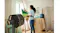A pedestal fan is positioned in an art studio while a person paints on a canvas in the background A pedestal fan is positioned in an art studio while a person paints on a canvas in the background