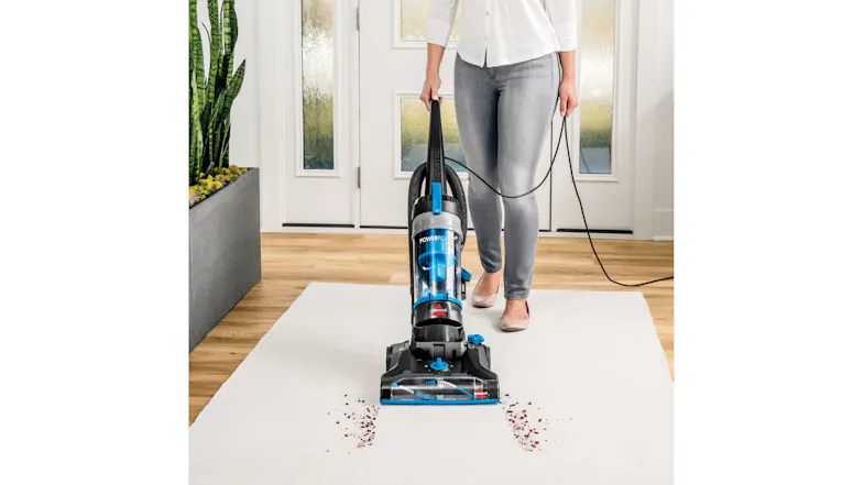 A person vacuuming debris on a white rug using a black and blue upright vacuum A person vacuuming debris on a white rug using a black and blue upright vacuum