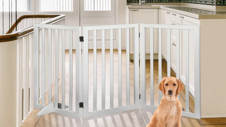 A white three‑panel pet gate is placed at a kitchen entrance, with a dog sitting in front of it A white three‑panel pet gate is placed at a kitchen entrance, with a dog sitting in front of it