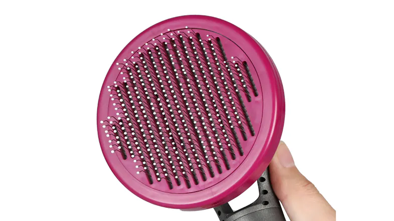 Close-up of a round pet slicker brush with fine metal pins, held in a hand to show the surface detail of the bristles Close-up of a round pet slicker brush with fine metal pins, held in a hand to show the surface detail of the bristles