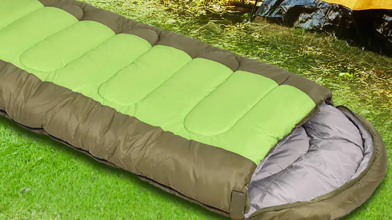 A green and brown sleeping bag with a hood lay on the grass outdoors near a tent A green and brown sleeping bag with a hood lay on the grass outdoors near a tent