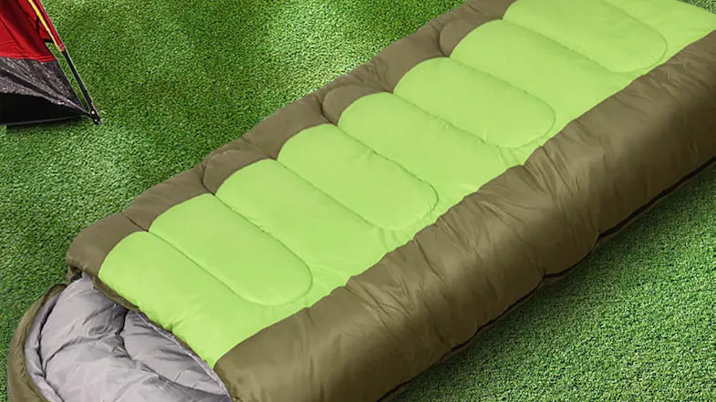 Top view of a green and brown sleeping bag on grass beside a camping tent Top view of a green and brown sleeping bag on grass beside a camping tent