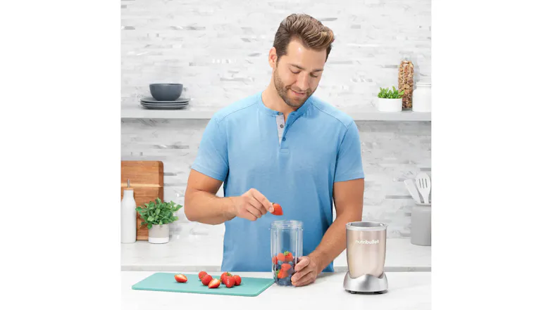 Person loading fresh strawberries into a blender cup for a smoothie beside a NutriBullet Person loading fresh strawberries into a blender cup for a smoothie beside a NutriBullet